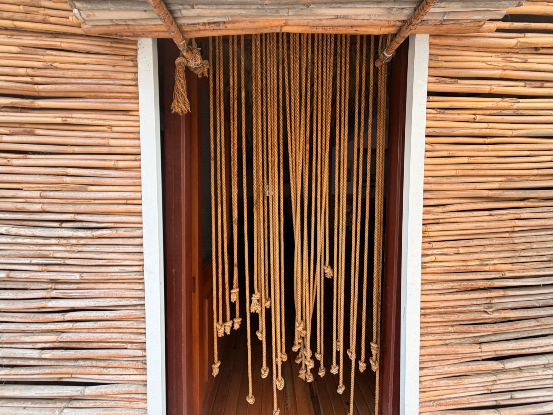 Bambu kaplı duvarlar arasında, halat perdeli hamam girişi